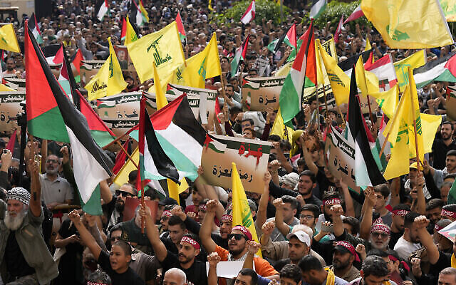 أنصار حزب الله يلوحون بالأعلام اللبنانية والفلسطينية ورايات المنظمة ويحملون لافتات مؤيدة لغزة خلال احتجاج لإظهار تضامنهم مع الفلسطينيين، في الضاحية الجنوبية في بيروت، لبنان، الجمعة، 13 أكتوبر، 2023. (AP/Hussein Malla)