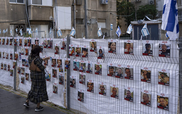 امرأة تنظر إلى صور رهائن محتجزين في غزة معلقة في رمات غان، 22 نوفمبر، 2023. (AP Photo/Oded Balilty)