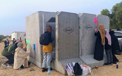 متطوعون بدو يقومون بطلاء ملجأ خرساني مضاد للصواريخ تم تركيبه في اليوم السابق في قرية أم الحيران غير المعترف بها في جنوب إسرائيل،  7 ديسمبر، 2023. (Gianluca Pacchiani/Times of Israel)