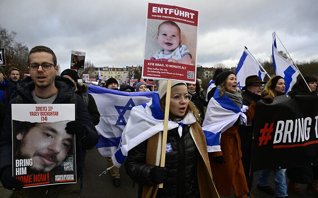متظاهرون يعرضون لافتات عليها صور الرهينتين الإسرائيليتين ياغيف بوخشتاب (يسار الصورة) وكفير بيباس خلال مسيرة لإحياء ذكرى  مرور 100 يوم على احتجاز الرهائن الإسرائيليين في غزة، في 14 يناير، 2024 في برلين. (John MacDougall / AFP)