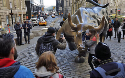 أشخاص يلتقطون صورًا مع تمثال الثور الهائج في الحي المالي في نيويورك، الأحد، 15 مارس، 2020. (AP Photo / Richard Drew)