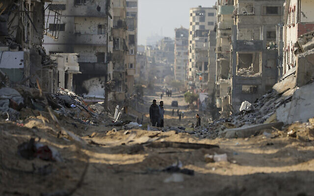 وسط الحرب بين إسرائيل وحماس، فلسطينيون يسيرون بين أنقاض المباني المدمرة على الطريق الرئيسي في مدينة غزة، 2 يناير، 2024. (AP Photo/Mohammed Hajjar)