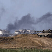 دخان متصاعد في قطاع غزة خلف دبابة إسرائيلية بالقرب من الحدود بين إسرائيل وغزة، 13 مايو، 2024. (AP/Leo Correa)