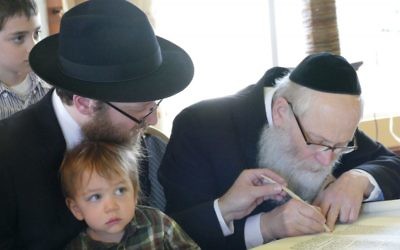 Rabbi Zalman Charytan, who leads Chabad of West Cobb, lends a hand to the sofer, Rabbi Moshe Klein.