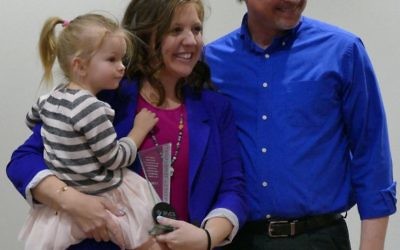 Chris Greer, last year’s winner of the Stacy G. Fialkow Staff Appreciation Award, stands with this year’s winner, Ashley Semerenko, holding daughter Vivian, after surprising her with the announcement.