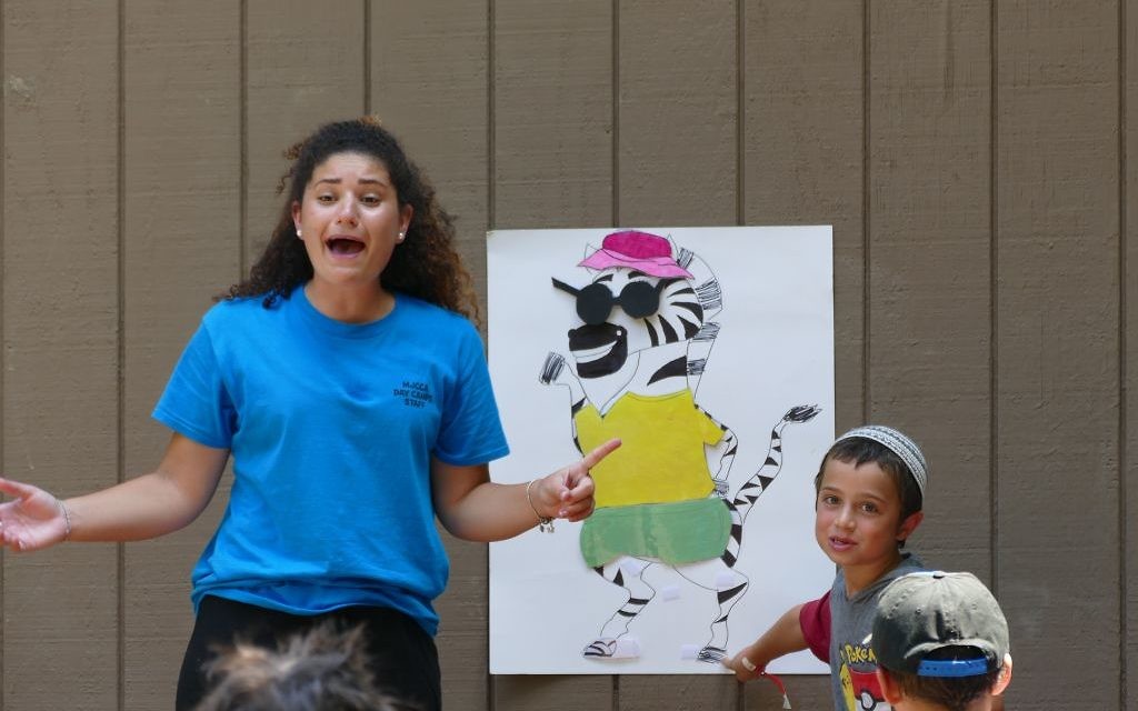 Israeli counselor Sapir Beresi leads campers in the Marcus JCC’s Hebrew immersion day camp program in a game in which they must put articles of clothing on a zebra and say the items’ names in Hebrew.
