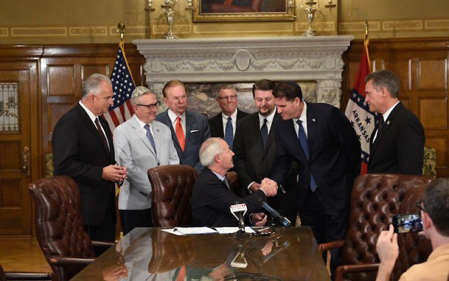 Arkansas Gov. Asa Hutchinson (seated) is congratulated by Ambassador Ron Dermer after signing a pair of pro-Israel bills Aug. 14.