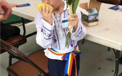 Kindergartner Michael Manoloche, wearing an outfit customary to Romania, practices the universal Jewish Sukkot custom of shaking the lulav and etrog.