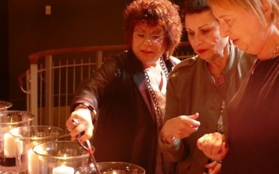 Abe Besser’s nieces (from left) Peggy Klug, Gina Karp and Susan Scheinfeld light a candle during the Kristallnacht commemoration.