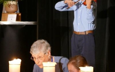 While Joshua Sampson provides accompaniment on the violin and Eden Guggenheim stands at her side, Holocaust survivor Suzan Tibor lights one of the memorial candles at the start of the Am Yisrael Chai ceremony.