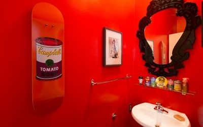 The powder room pays homage to Andy Warhol. The shocking paint color is Benjamin Moore’s Simply Red. The autograph on the David Bowie photograph is addressed to Buxbaum — “Thanks for the use of your gaffe (and the sounds)” — after Bowie spent the day at his apartment. The mirror is a Venetian replica. (Photo by Duane Stork)