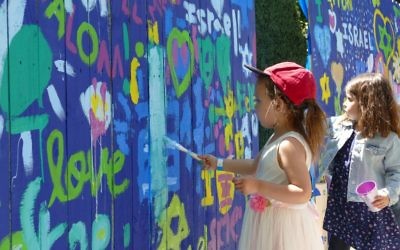Young artists decorate a fence with messages of love for Israel.