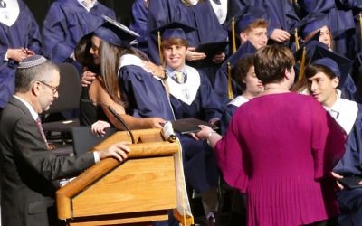 Science teacher Nicole Brite manages to hug one student while passing the diploma for the next graduate to Principal Shlaina Van Dyke as Associate Head of School Paul Ginburg reads the names.
