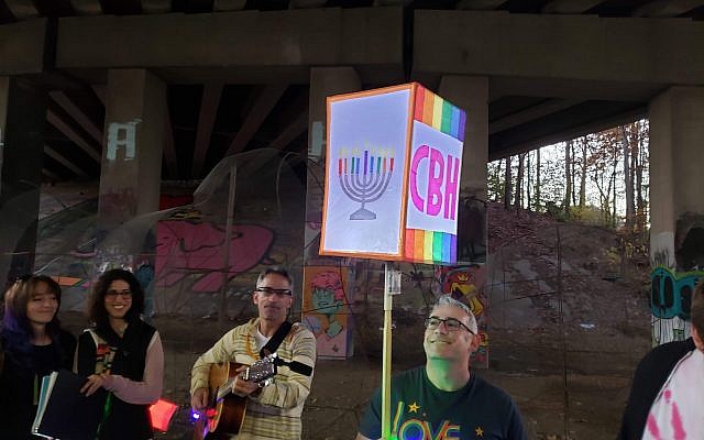 Congregation Bet Haverim Rabbi Joshua Lesser held aloft a lighted CBH sign as congregant Brad Davidorf, on guitar, led congregants in Chanukah songs, including the Ladino “Ocho Kandelikas.”