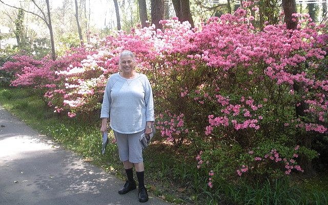 Judy in front of blooming flowers at their previous home.
