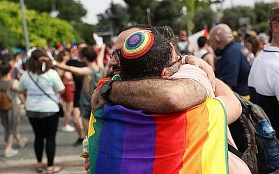 Two people wearing rainbow colors embrace at the parade.