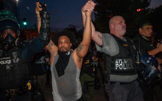Lieutenant Knapp of the Atlanta police holds hands and marches with a protester in an attempt to get them to disband after a 9 p.m. curfew. Some protesters attempted to get others to leave Sunday, May 31