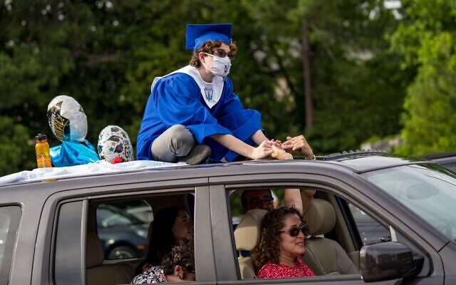 Ari Slomka sits on the roof of the family car holding hands with his parents.