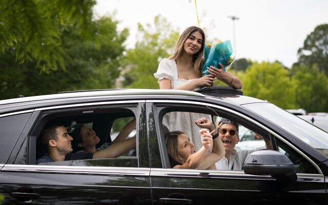 Avia Zaken peeks out through the sunroof with a bouquet as her parents, Ronita and Yaron, and family cheer her on.