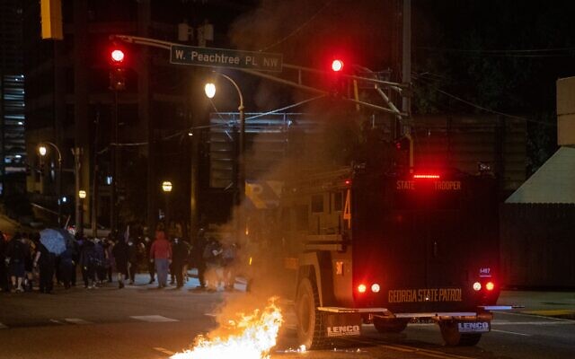A Georgia State Patrol vehicle moves towards protesters as an officer fires rubber bullets and pushes past a fire caused by a Molotov cocktail. // AJT’s Nathan Posner