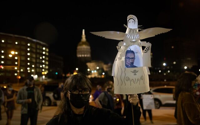 A mourner holds a cutout angel with the late Justice Ginsburg pictured inside, with a sign honoring the late justice visible in the background at a candlelight vigil in the late justice's honor. // Nathan Posner for the AJT.