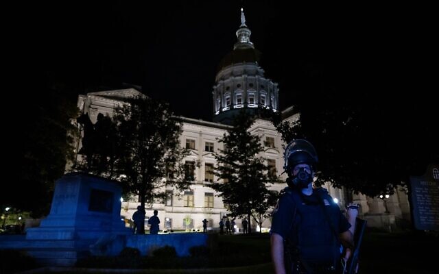 A state patrol officer is illuminated by the lights of a patrol car, with the Georgia State Capitol building seen in the background. // Nathan Posner for the AJT.