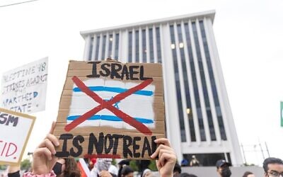 A protestor holds a sign saying “Israel is not real” during a pro-Palestine protest, with the Israeli consulate in the background. // Nathan Posner for the AJT