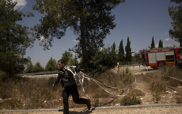An Israeli first responder runs with hoses while battling wildfires for the second day near Shoresh, on the outskirts of Jerusalem, Aug. 16, 2021 (AP Photo/Maya Alleruzzo)