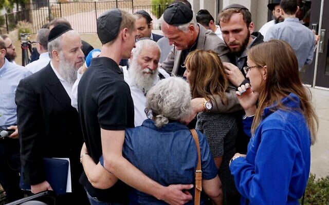 Rabbi Yisroel Goldstein, center, surrounded by his congregants on Sunday outside the Chabad of Poway. Rabbi Goldstein was shot in an attack at the synagogue on Saturday. // Photo Credit: Sandy Huffaker/Agence France-Presse — Getty Images