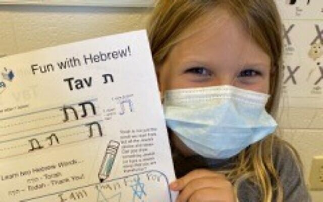 A student proudly shows of her Hebrew alphabet worksheet.