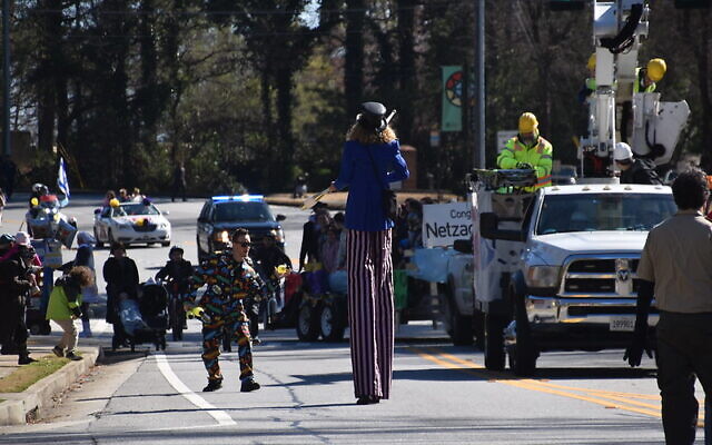 A stilt-walking juggler entertains the crowd alongside Beth Jacob eruv repair truck.
