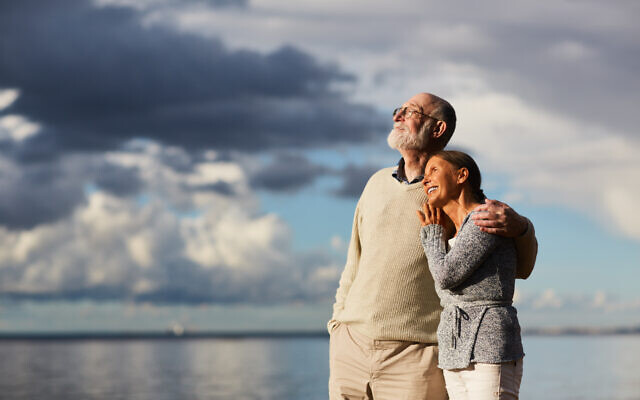 Amorous seniors standing by water against stormy sky and enjoying sundown