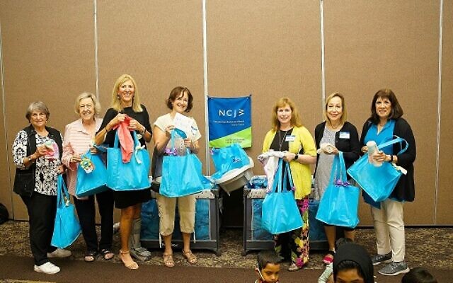 Photo of NCJW leaders holding up gift bags for mothers and mothers-to-be at baby shower.