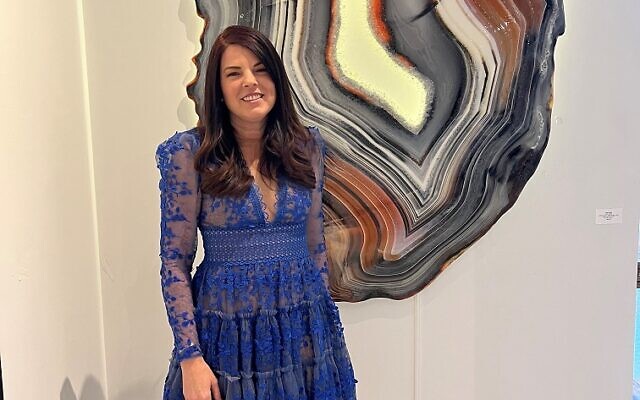 Amy Rader, adorned in sapphire lace, stands by her agate painting.
