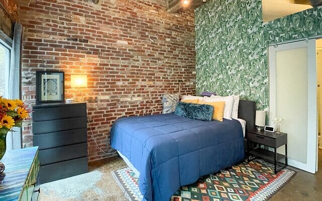 Primary bedroom has palm frond wallpaper and glass art by Janko that blends with the original exposed brick walls.