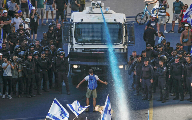 A protester stands in front of a police water cannon being used to disperse demonstrators blocking a road during a protest against moves by Prime Minister Benjamin Netanyahu's government to overhaul the judicial system, in Jerusalem, July 24, 2023. (AP/Ariel Schalit)