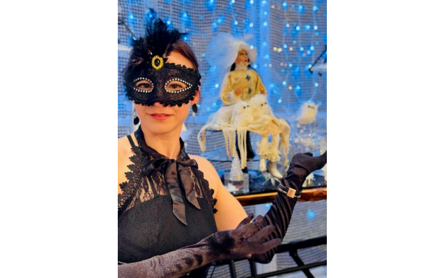 A masquerade queen poses by a fantasy scene.