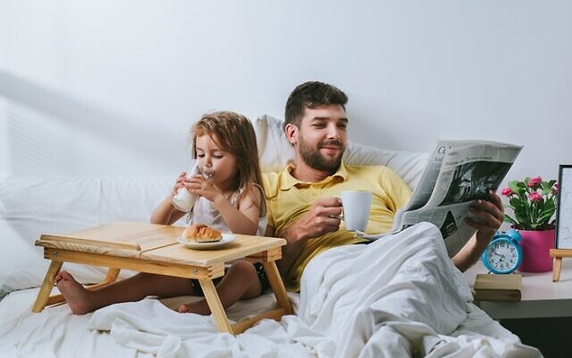 Father and daughter having breakfast in bed. Father drinking coffee and reading newspapper