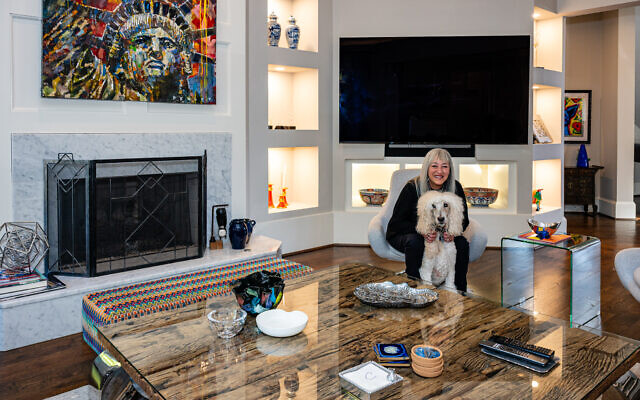 Artist Cheryl Henos poses with poodle, Raffi, near a Steve Penley painting over the fireplace. The cocktail table is composed of reclaimed railroad ties.   