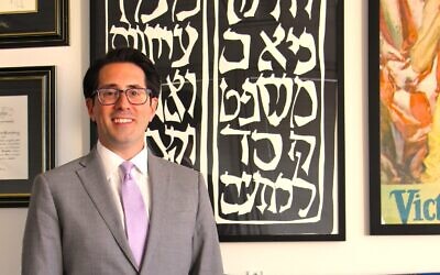 Teddy Hertzberg, known as fast, firm, and fair, stands by his office poster, a woodcut depicting Micah 6:8 to “do justice, love kindness, and walk humbly with your God.”