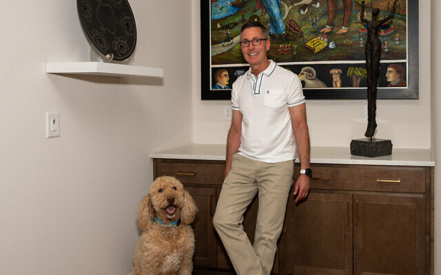 Gary and goldendoodle Bennie pose in front of Lamar Smith’s dreamlike painting of Jewish symbolism, a seven-branched menorah, the Akedah, Adam and Eve and Jacob’s Ladder.  