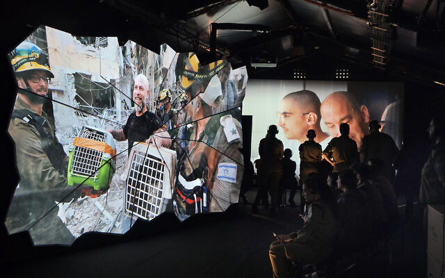 IDF Soldiers are viewing the exhibit; in one side volunteers saving animals from the site and the other is a picture of former hostage Rom Braslavski, embraced by his father.