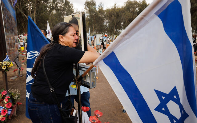 Rita, the mother of Officer Elior Yifrach z”l, an undercover detective, embraces his photograph in tears and agony, holding a post bearing the Israeli flag at Re’im, the site of the Nova Festival.