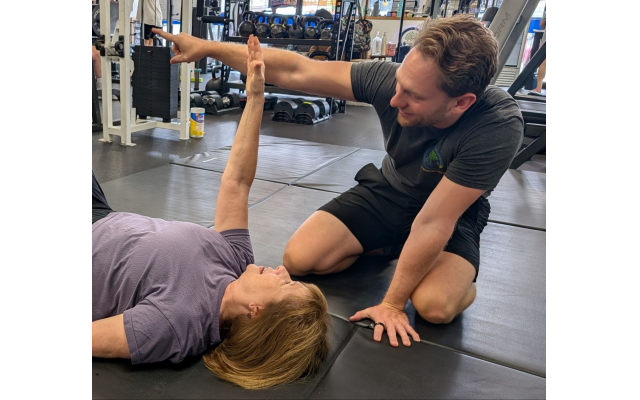 Alex Mitchell, founder of Stronger Now Gym in Sandy Springs, instructs a client on floor mat exercises.