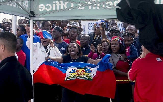 Haitians line the sidewalks as President Donald Trump's motorcade returns to Mar-a-Lago in West Palm Beach, Florida, on January 15, 2018. (AP Photo/Andrew Harnik)