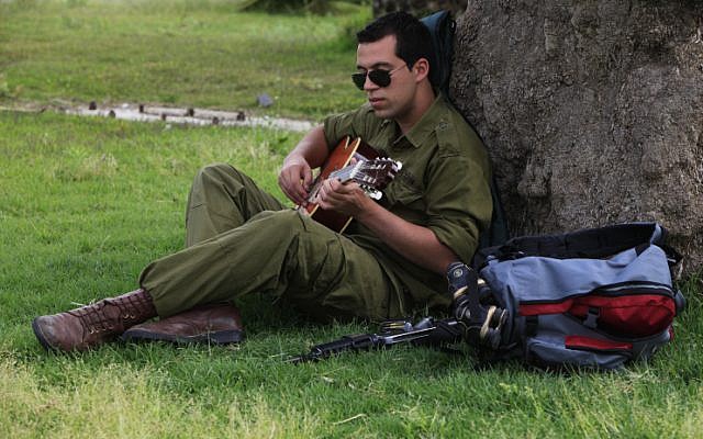 An Israeli soldier plays his guitar while he waiting for a bus. (photo credit: Tsafrir Abayov/Flash90)