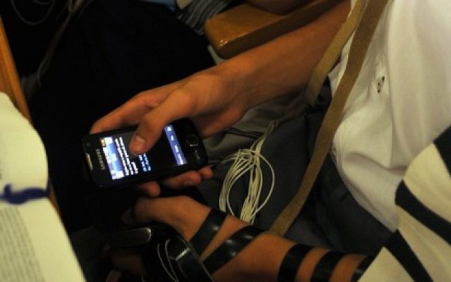 Young Jew plays on a cellphone in a synagogue during morning prayers. (Serge Attal/Flash90)