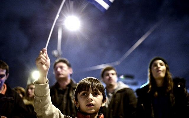 A young child waves the national flag as crowds gather in front of the Greek parliament in Athens on February 5, 2015 in support of the new anti-austerity government's efforts to renegotiate Greece's international loans (Photo credit: Louisa Gouliamaki/AFP)