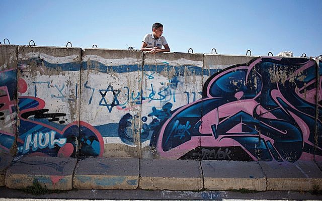 A Palestinian boy looks behind a wall separating Jewish  (Jewish News AP Photo/Ariel Schalit)