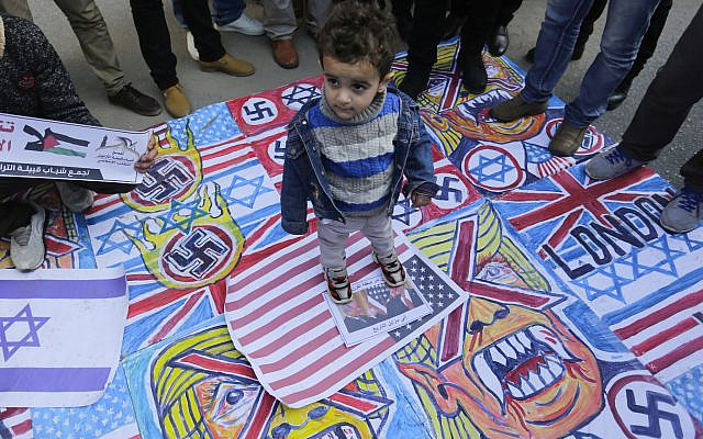 A Palestinian child stands on the illustrations of the British Union flag, the Israeli flag, and an American flag during a protest against the American peace plan in the Middle East, in Gaza City. (Photo by Mahmoud Issa / SOPA Images/Sipa USA via Jewish News)